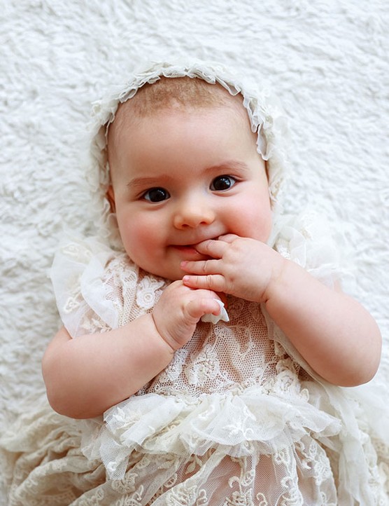 baby girl lying down wearing an old fashioned dress and bonnet