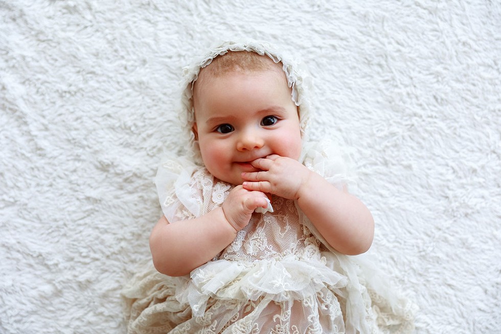 little child lies on the bed and smiles baby girl lying down wearing an old fashioned dress and bonnet
