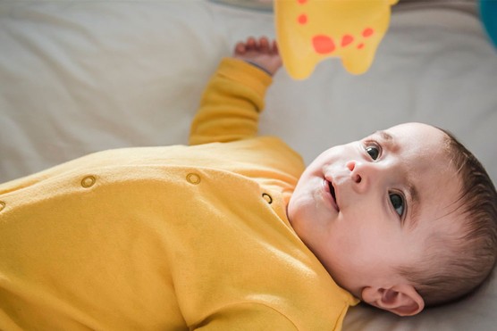 baby lying on back and staring at colourful toy dangling from play gym
