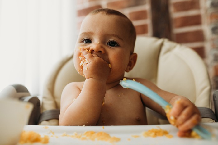 Funny baby eating healthy food on kitchen baby in high chair feeding itself while weaning