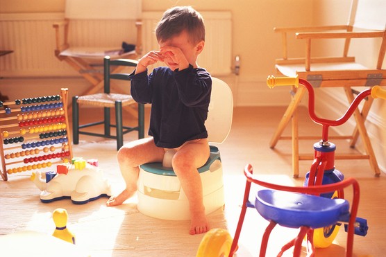 little boy crying while using potty in a room surrounded by toys