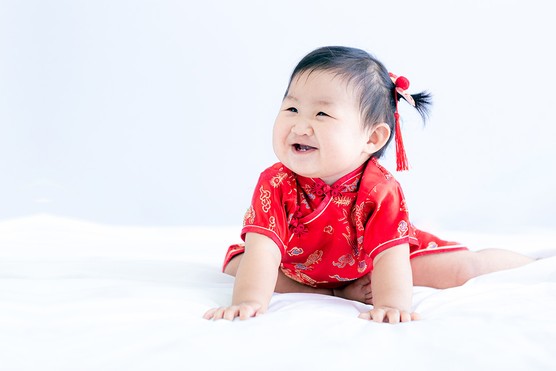 Chinese baby girl in traditional dress sitting on bed