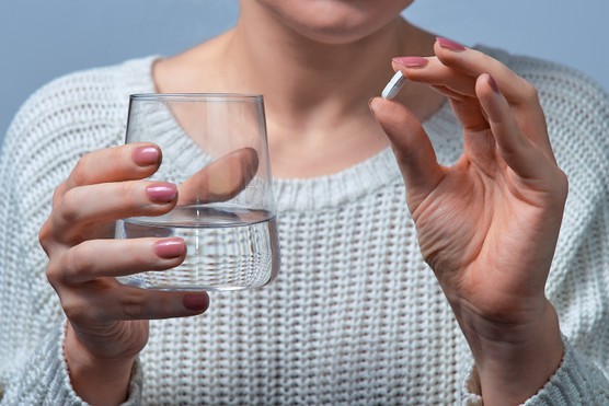 woman holding a pill and a glass of water