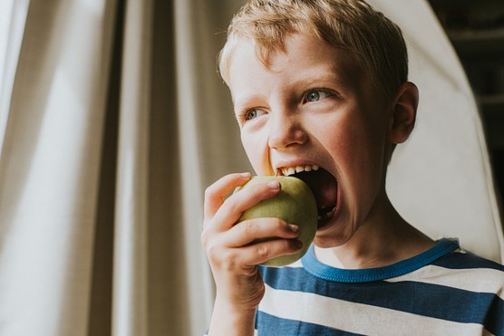 A boy taking a bite of a green apple.