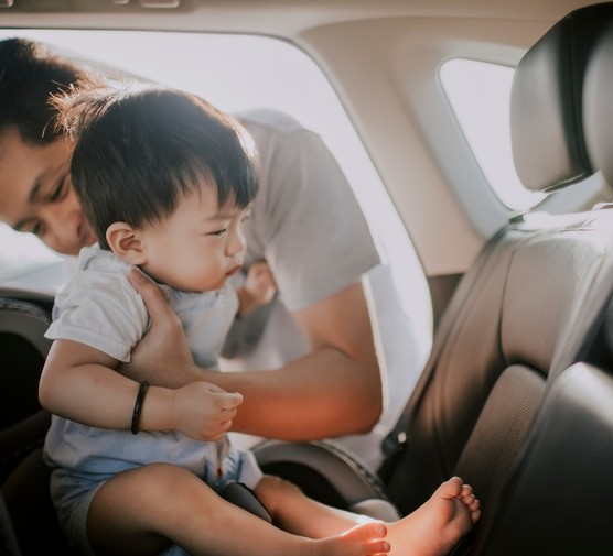 dad putting child into car seat in a car