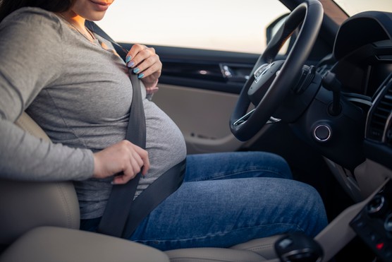Pregnant woman adjusting seatbelt in a car.