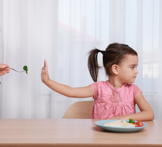Cute little girl refusing to eat vegetables at home