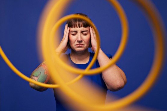 Woman with head in hands standing with eyes closed behind spiral cables against blue background