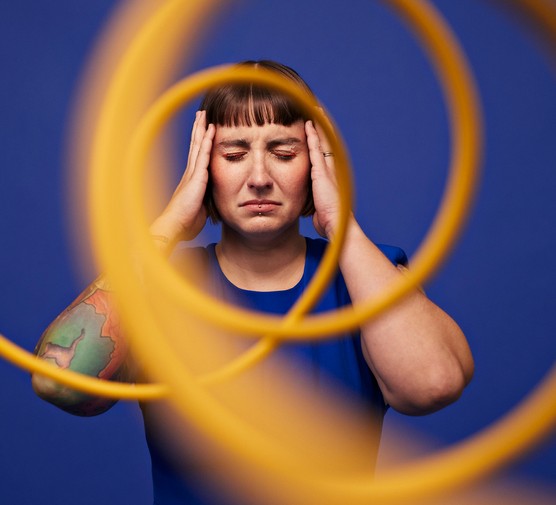 Woman with head in hands standing with eyes closed behind spiral cables against blue background