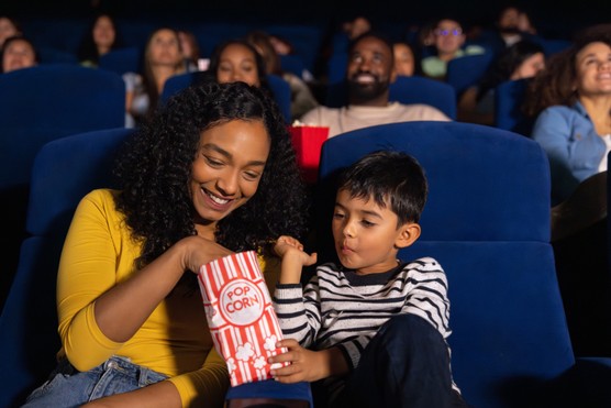 Loving Latin American mother and son eating popcorn while watching a movie at the theatre