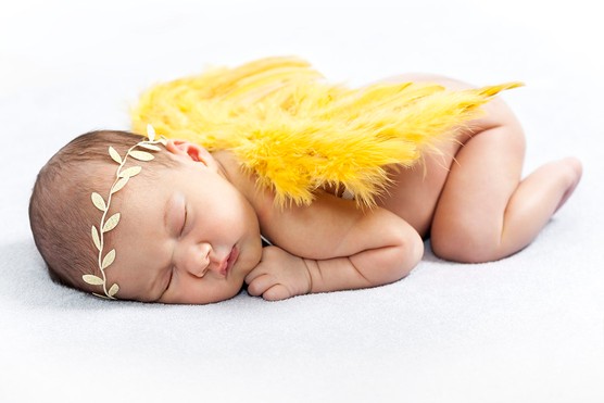 newborn baby dressed as a little angel with yellow wings and gold leaf crown