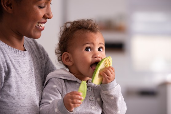 Portrait of mother and hungry baby eating an avocado. Child healthy eating.