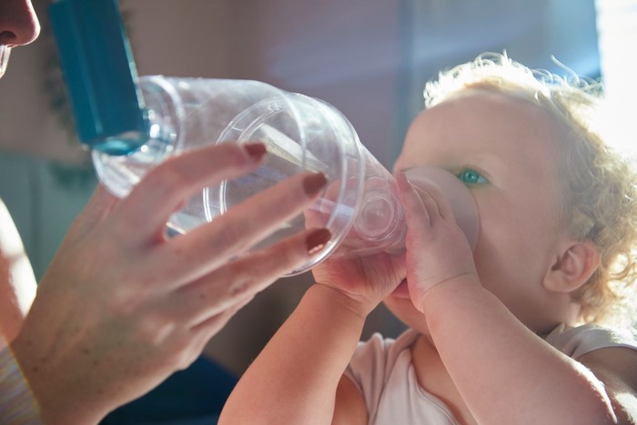 A toddler being given a dose of her asthma inhaler with a spacer