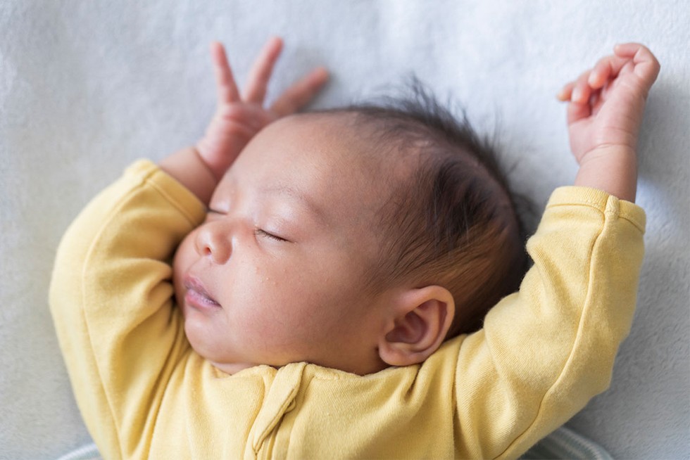top-unique-baby-boy-names baby boy in yellow sleep suit, asleep with arms up