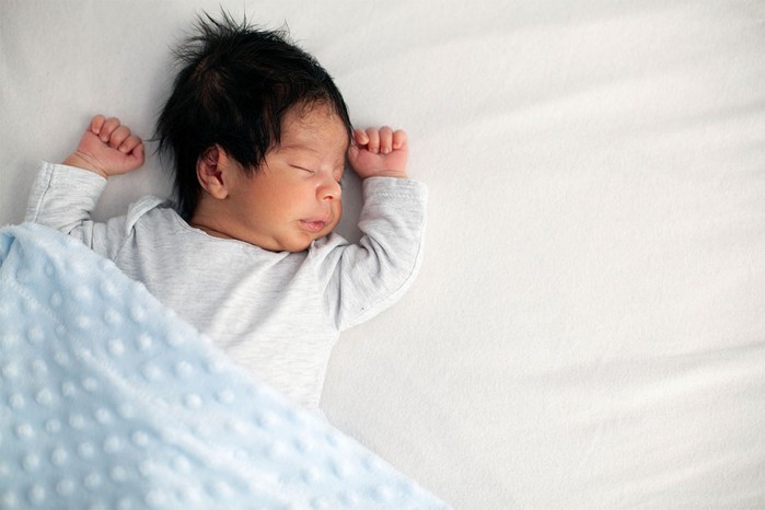 baby boy lying on a white sheet with blue blanket